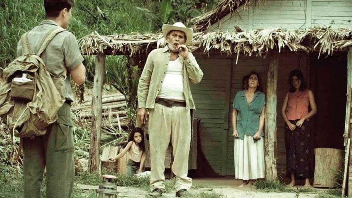 Two women and an older man stand in the doorway of a rustic house as a young man in uniform approaches them.