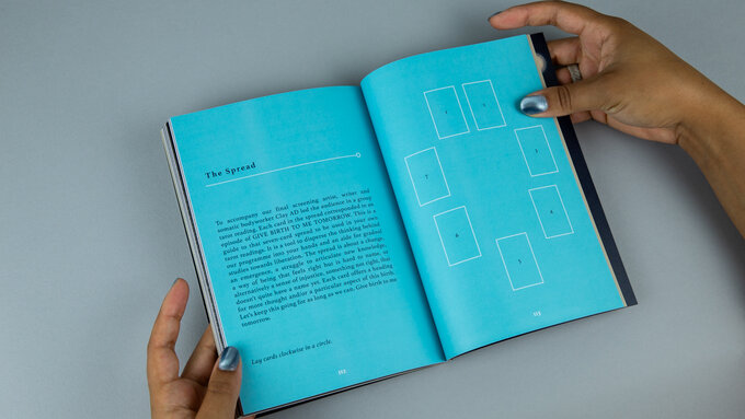 A pair of hands holds open an A5 size book. The interior is a bright cyan with white text.