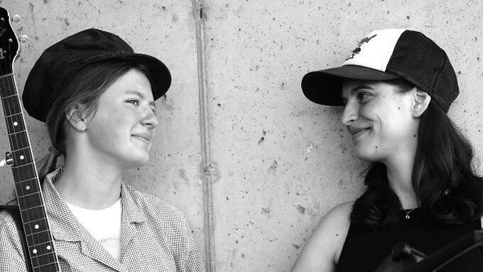 A black and white photo of two women, one holds a banjo and the other a fiddle.