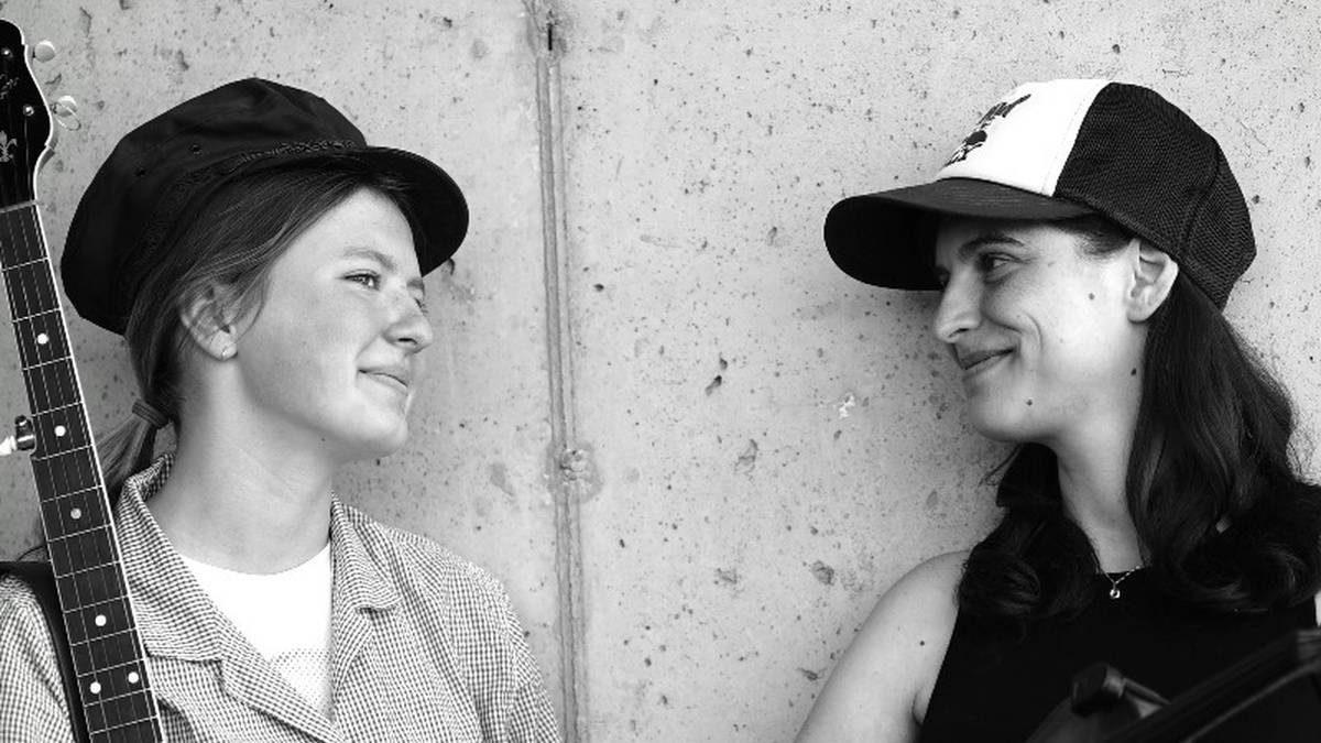 A black and white photo of two women, one holds a banjo and the other a fiddle.