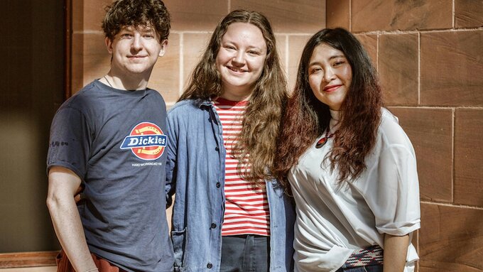 Three people stand facing the camera with arms across their shoulders.