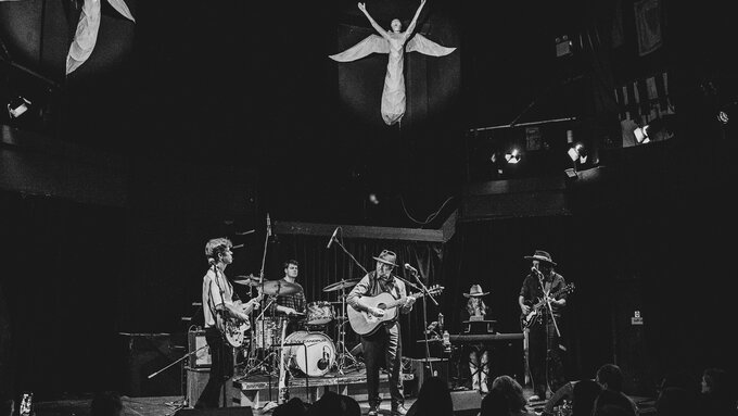 A black and white photo of Alan Fletcher and his band, two sculptures of angels appear to float above them.