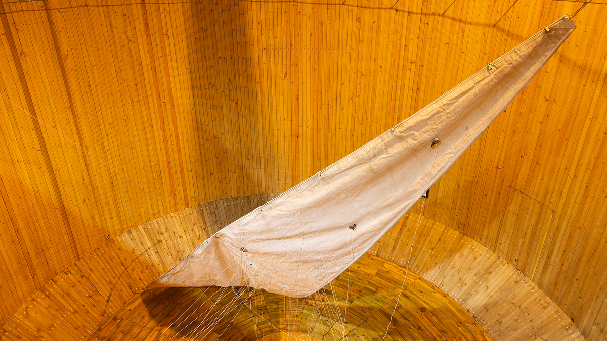 Large white sail-like fabric suspended with ropes inside a tall, circular wooden structure.