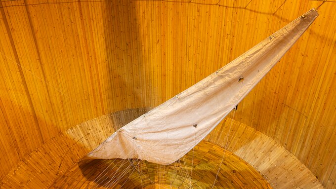 Large white sail-like fabric suspended with ropes inside a tall, circular wooden structure.