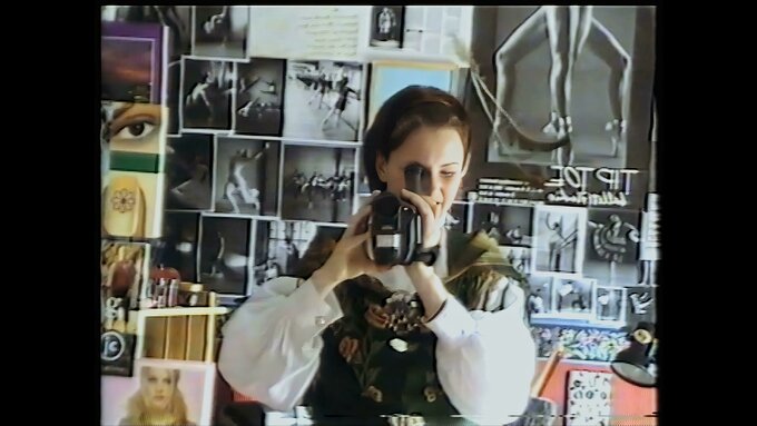 A still of a woman wearing medieval dress pointing a camcorder at a mirror.