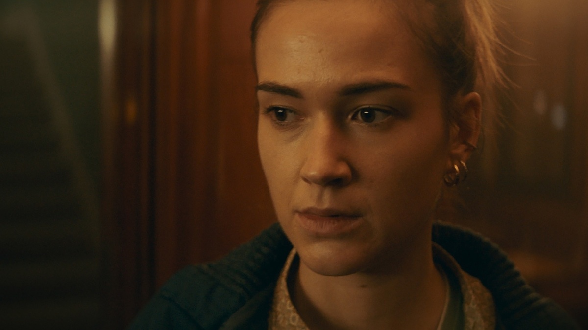 A blonde woman looking into the lens in a dark environment.