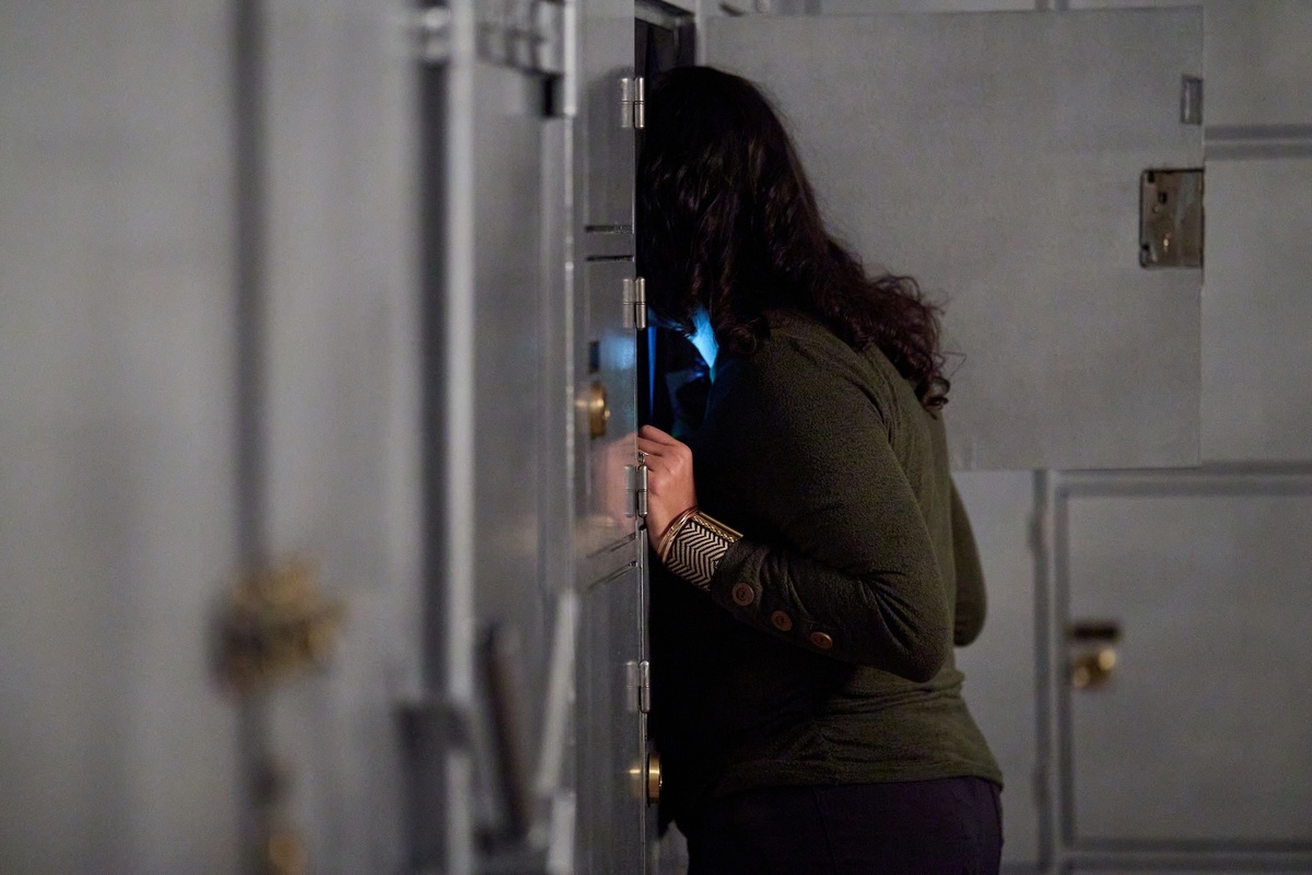 A person closely peering into an open locker embedded in a wall of grey metal compartments.