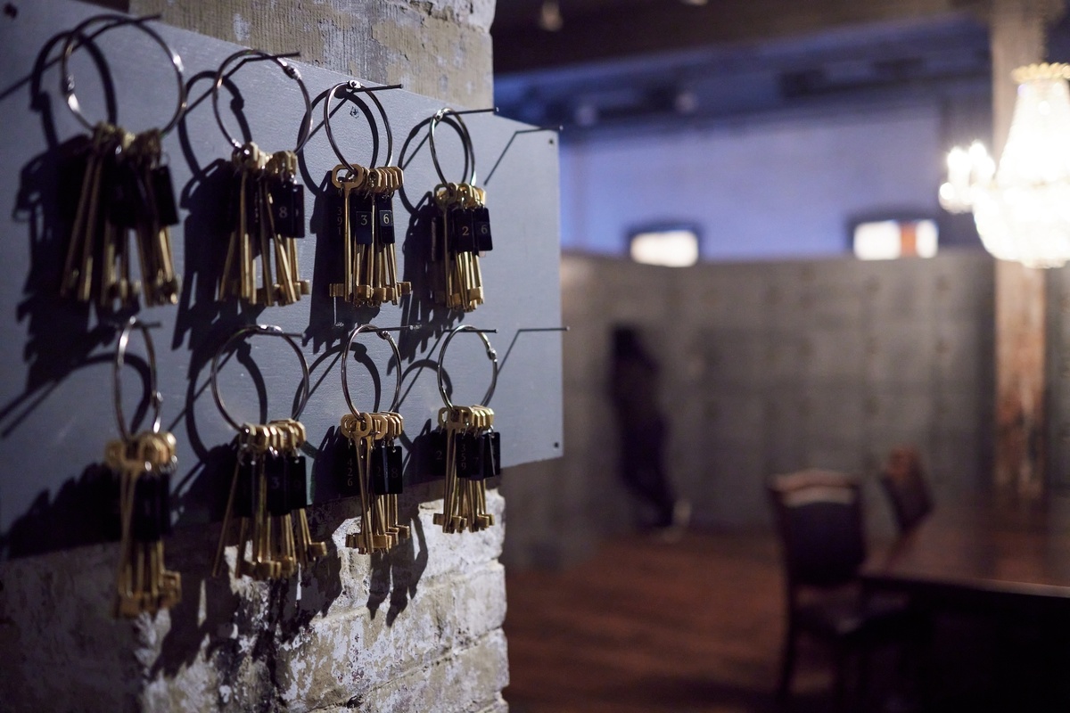 Close-up of brass keys hanging on rings mounted to a grey panel attached to a brick wall.