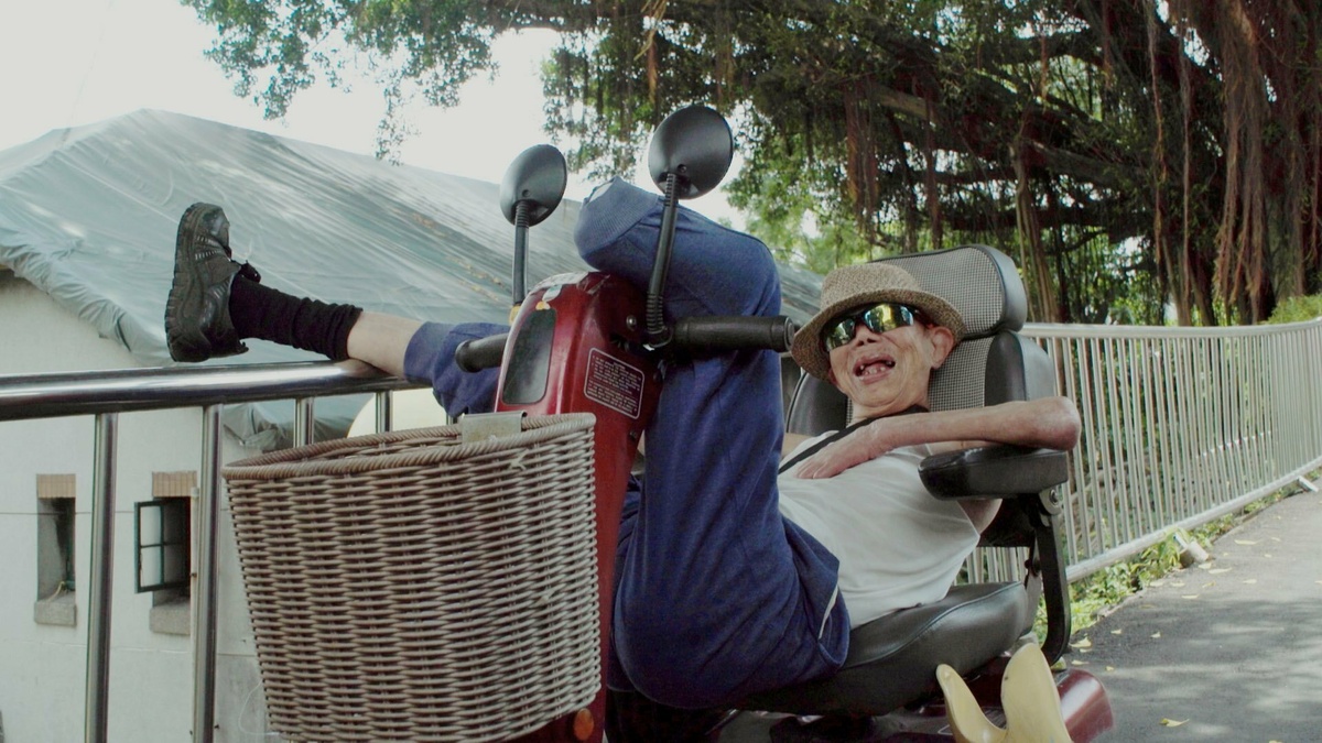 A sunlit shot of an elderly male resident of the Losheng Sanatorium, relaxing with his legs up on a motorized scooter.