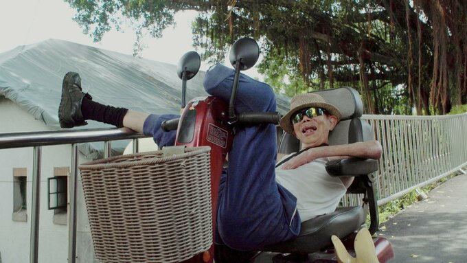 A sunlit shot of an elderly male resident of the Losheng Sanatorium, relaxing with his legs up on a motorized scooter.