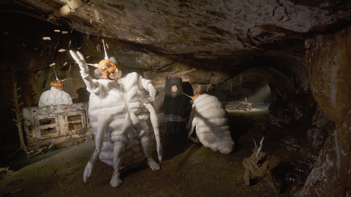 A person wearing a termite costume dancing in an underground set.