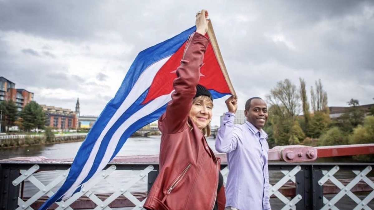 A woman and a man hold a Cuban flag, walking over a bridge in Glasgow.