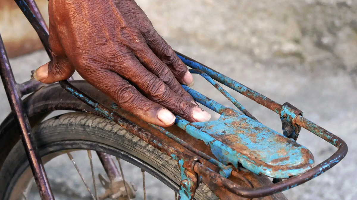 A person's hand touches the back of a rusty bike