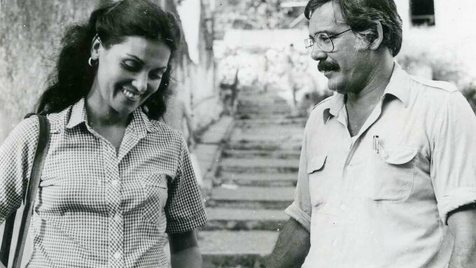 A woman and man stand at the bottom of some stairs. The woman is smiling.