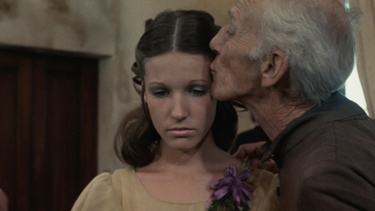 An older man kisses the head of a young woman, who seems upset.