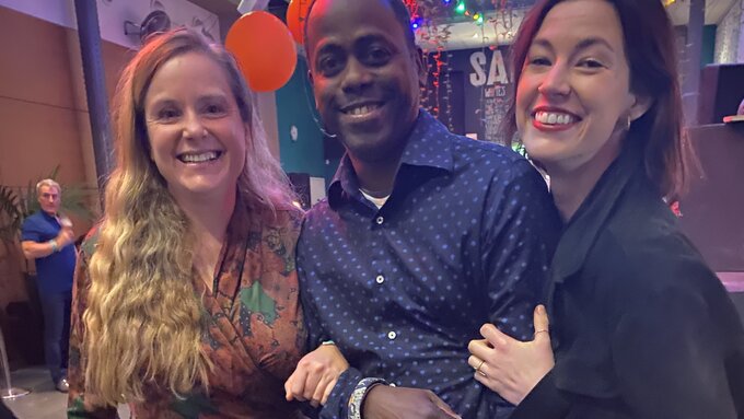 Three people stand together, linking arms and smiling