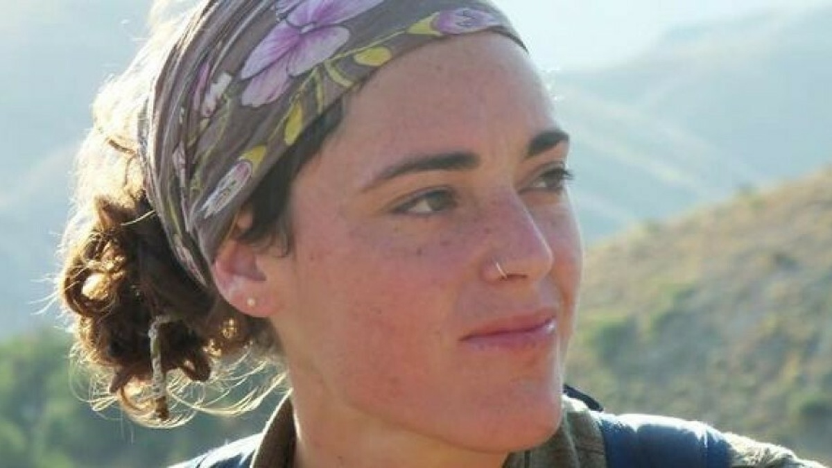 A young woman with a headscarf looks into the distance, with mountains behind her