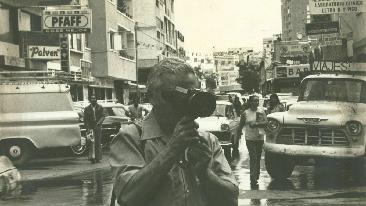 A person stands in a city street with an old camera