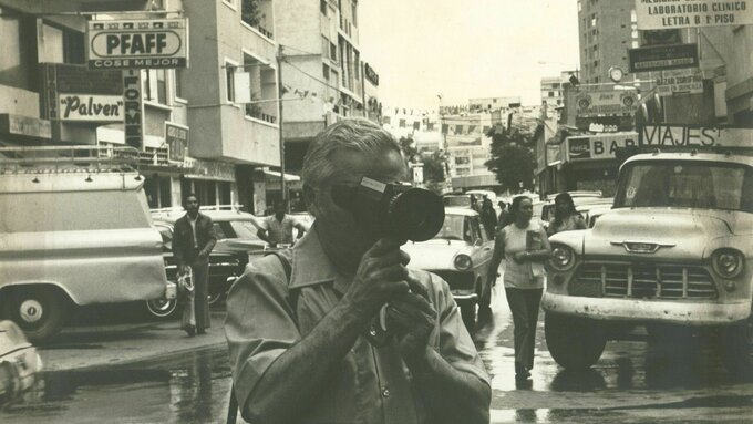 A person stands in a city street with an old camera