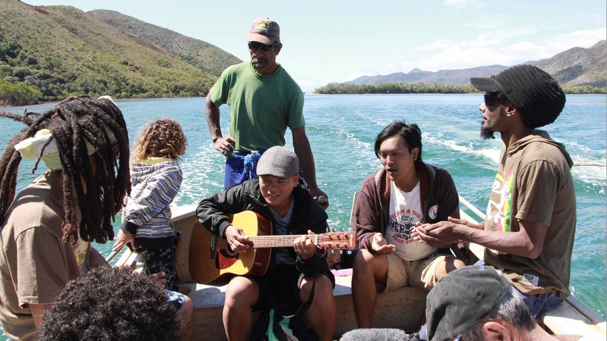 A wide, bright outdoor shot of a diverse group of seven people gathered on a small, motorized wooden boat on a lake.