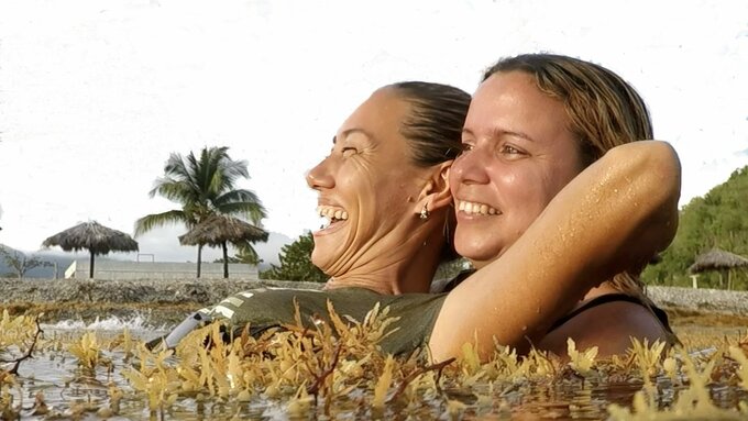 Two women hold each other in a lake, laughing