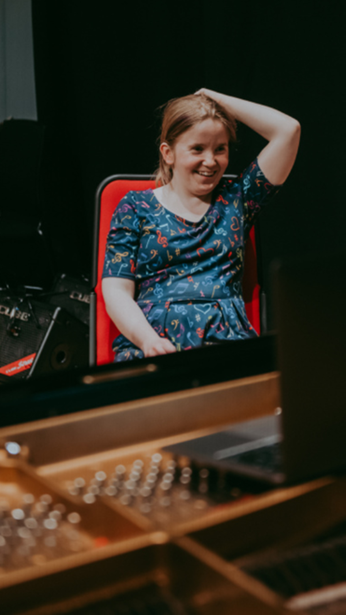 Sorcha sat with two microphones on stands beside her. She holds her phone into a mic as part of a performance.