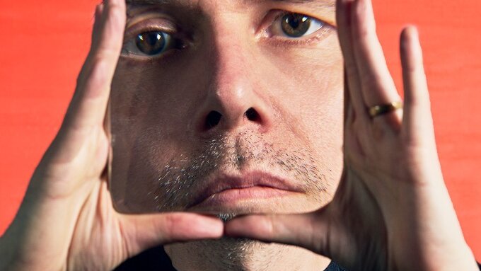 A highly edited photo of Clark, his head is extremely large and his hands frame his face.