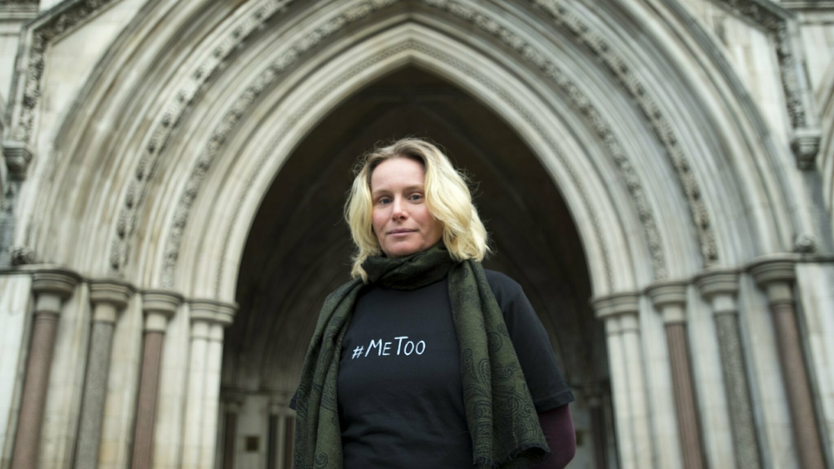 A blonde woman stood in front of a Cathedral doorway, she wears a t-shirt that says #metoo.