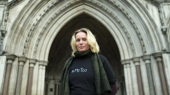 A blonde woman stood in front of a Cathedral doorway, she wears a t-shirt that says #metoo.