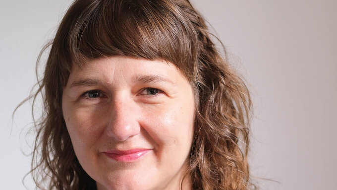 Clare Pollard a light skinned woman with a short fringe, green eyes and long curly hair.