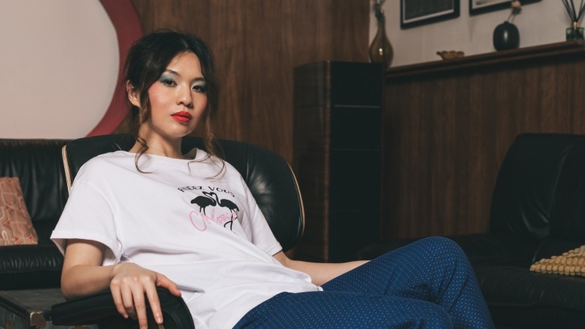 A woman with beige skin and long black wavy hair. She's reclining in a mid-century modern decorated house.