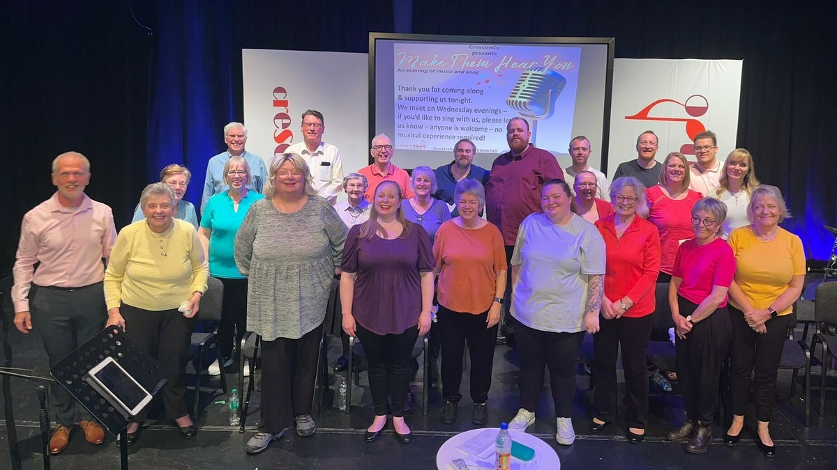 A group of people in a community choir smiling and singing as they prepare to perform.