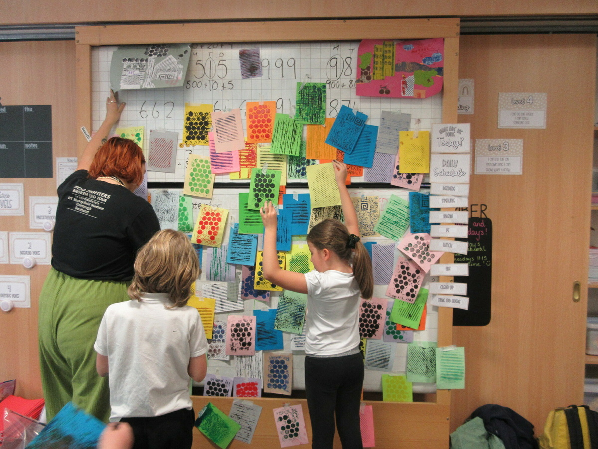 A photo of our young people coordinator, Sam Harley, and two primary school students pasting prints onto a wall.
