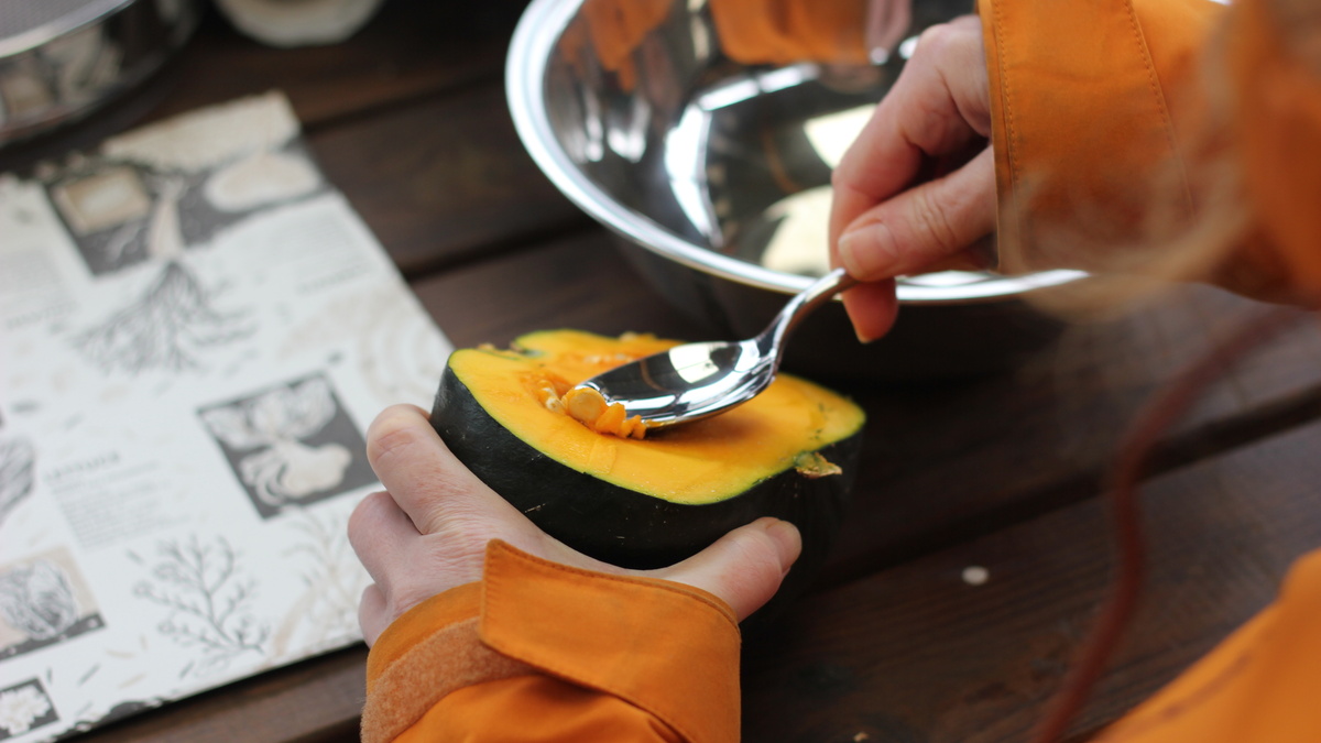 Hands with a spoon processing and cleaning squash seeds on a table.