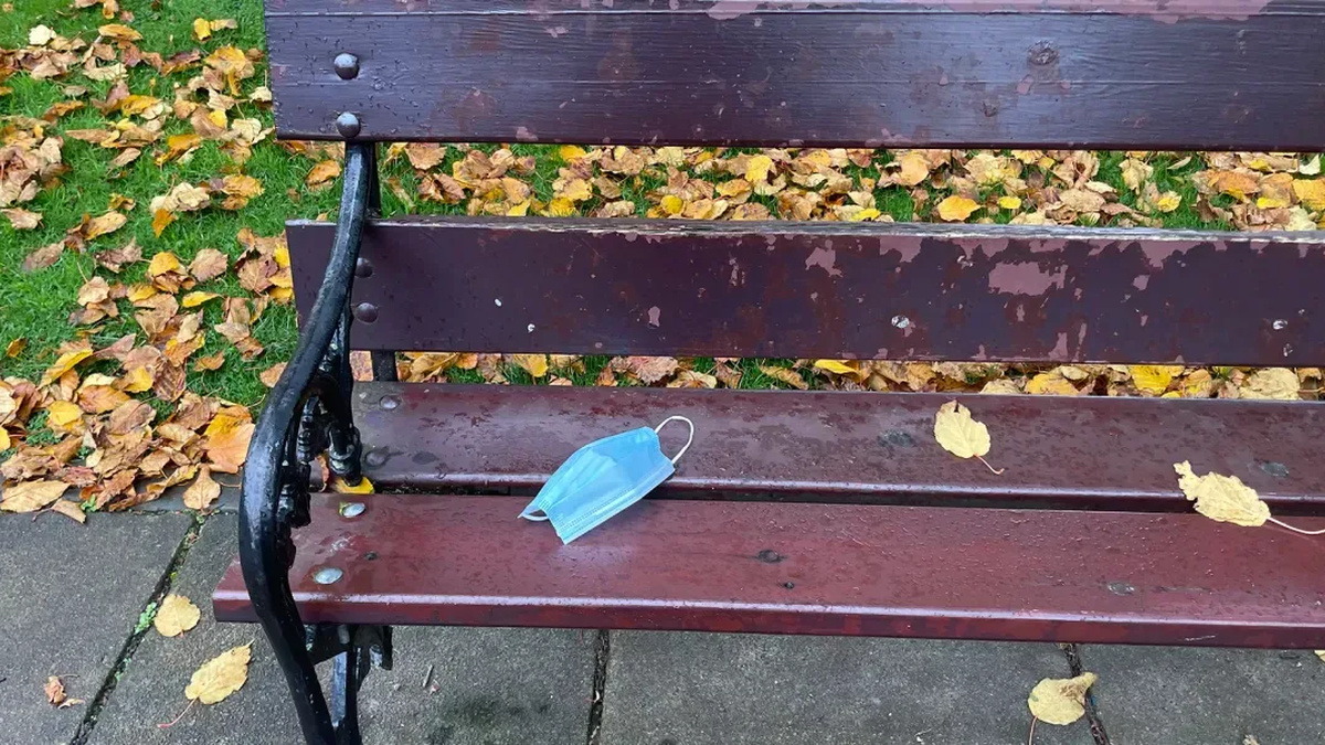 A park bench with a blue n95 face mask resting on it.