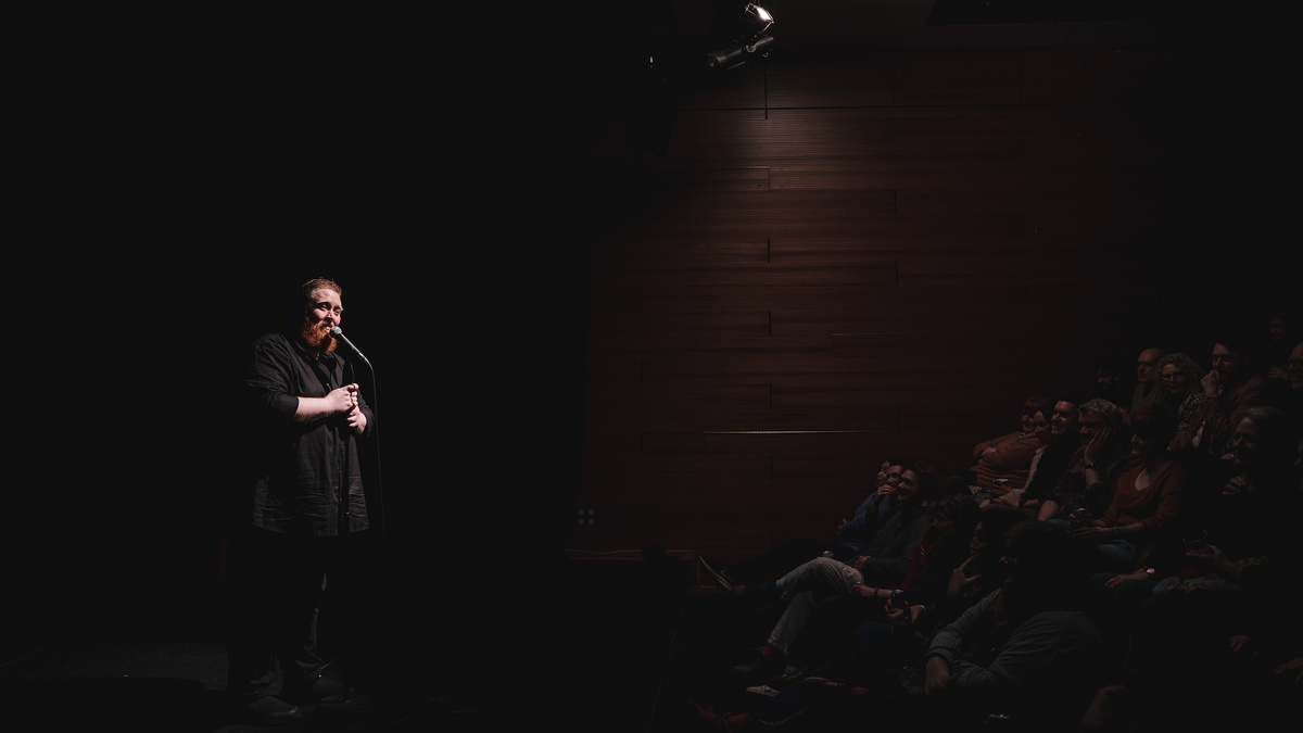 Kevin Mclean on stage hosting a Loud Poets show and the first few rows of audience