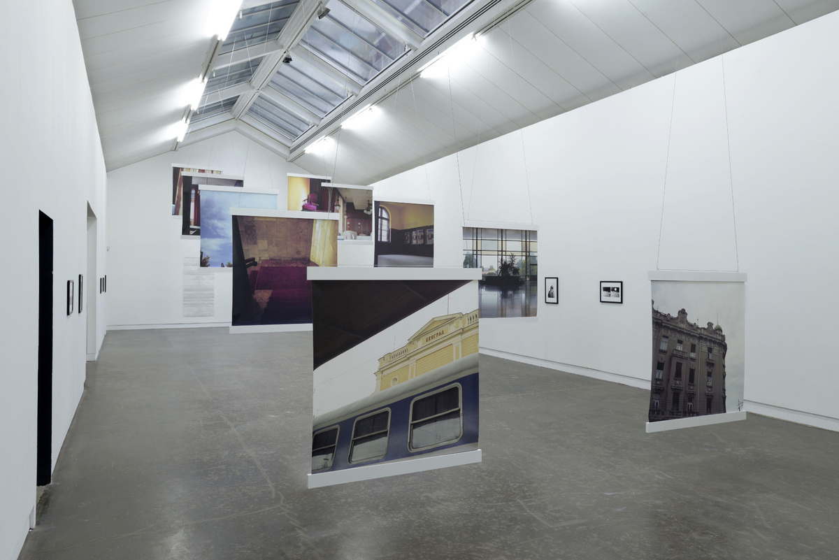 A photo of a wide wide well-lit gallery space, featuring large square canvas prints suspended from the ceiling.