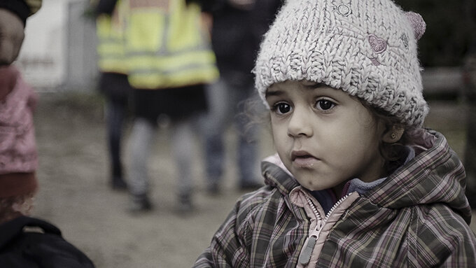 A young child standing in a crowd, with a wooly hat and tartan patterned jacket.