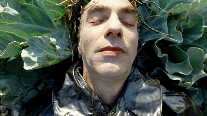 A still from The Garden featuring a close up of a person's face lying in foliage.