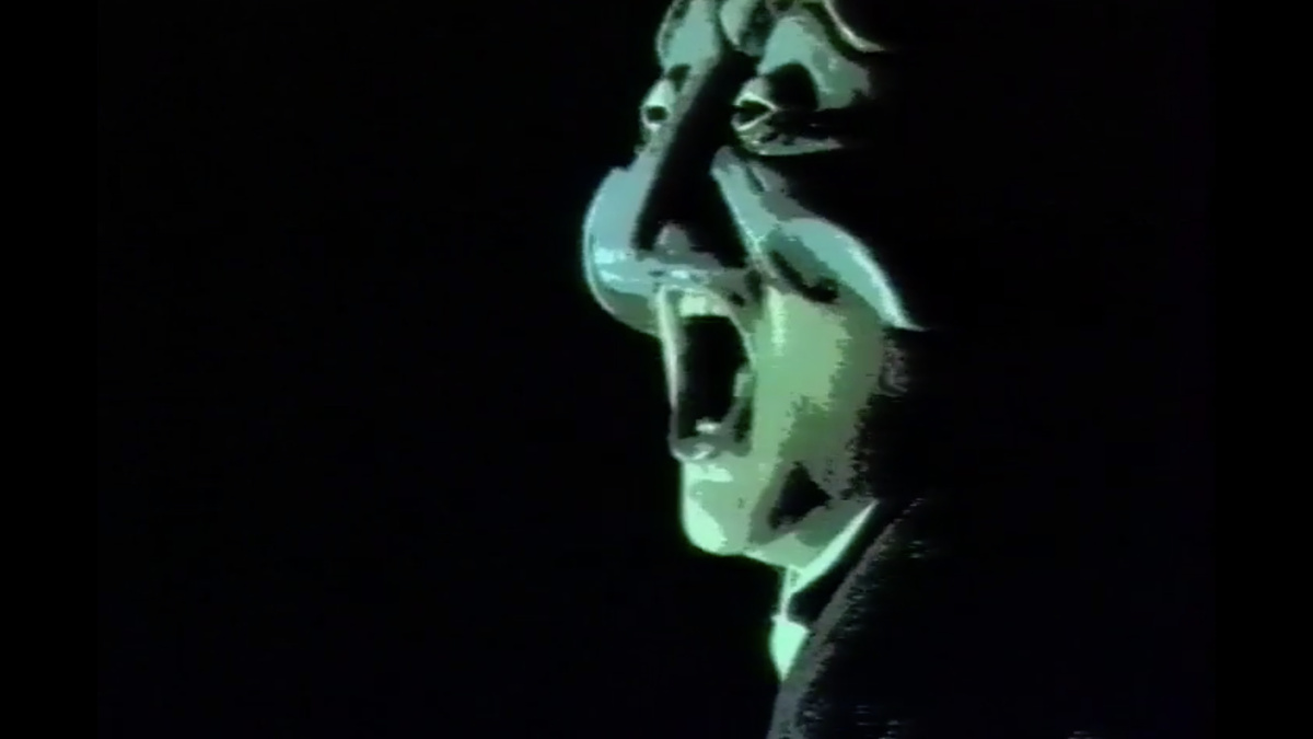 Close up of a green face, with mouth open, on a black background