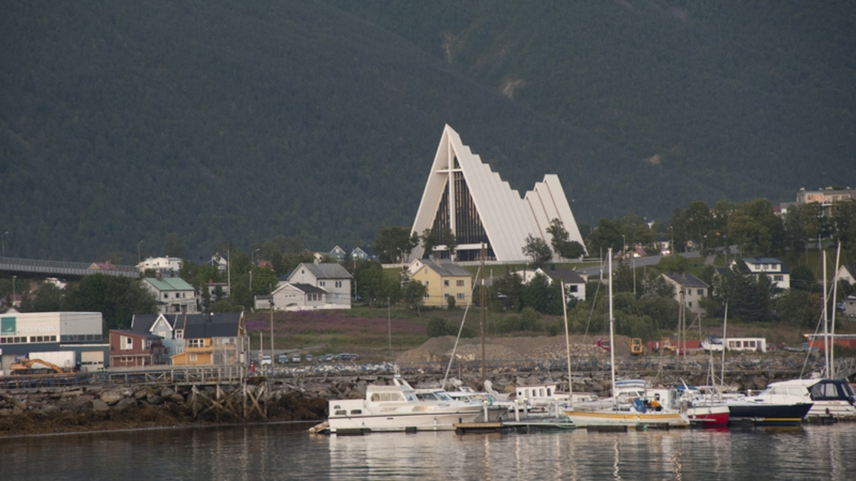 A landscape photograph of Tromsø, Norway. Boats sit on the water and there is a modern church building in the distance.