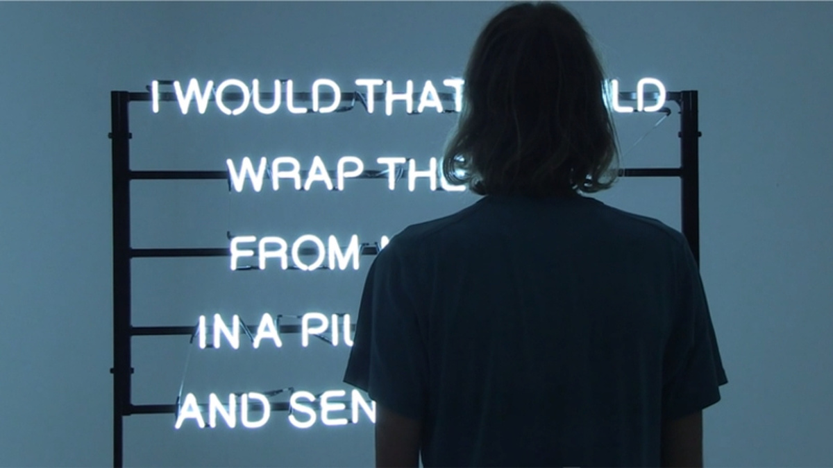 A person is silhouetted as they stand in front of a sign made up of neon lights in the form of words.