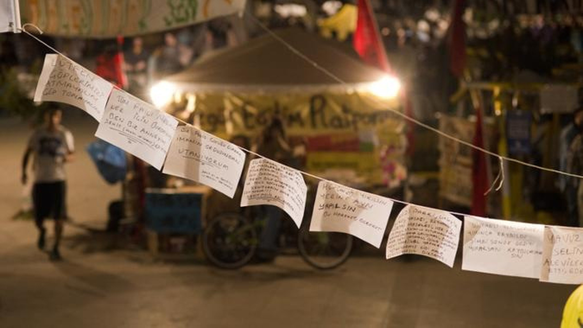 Several white squares of paper with written notes on them hang on a string in front of a city scene.