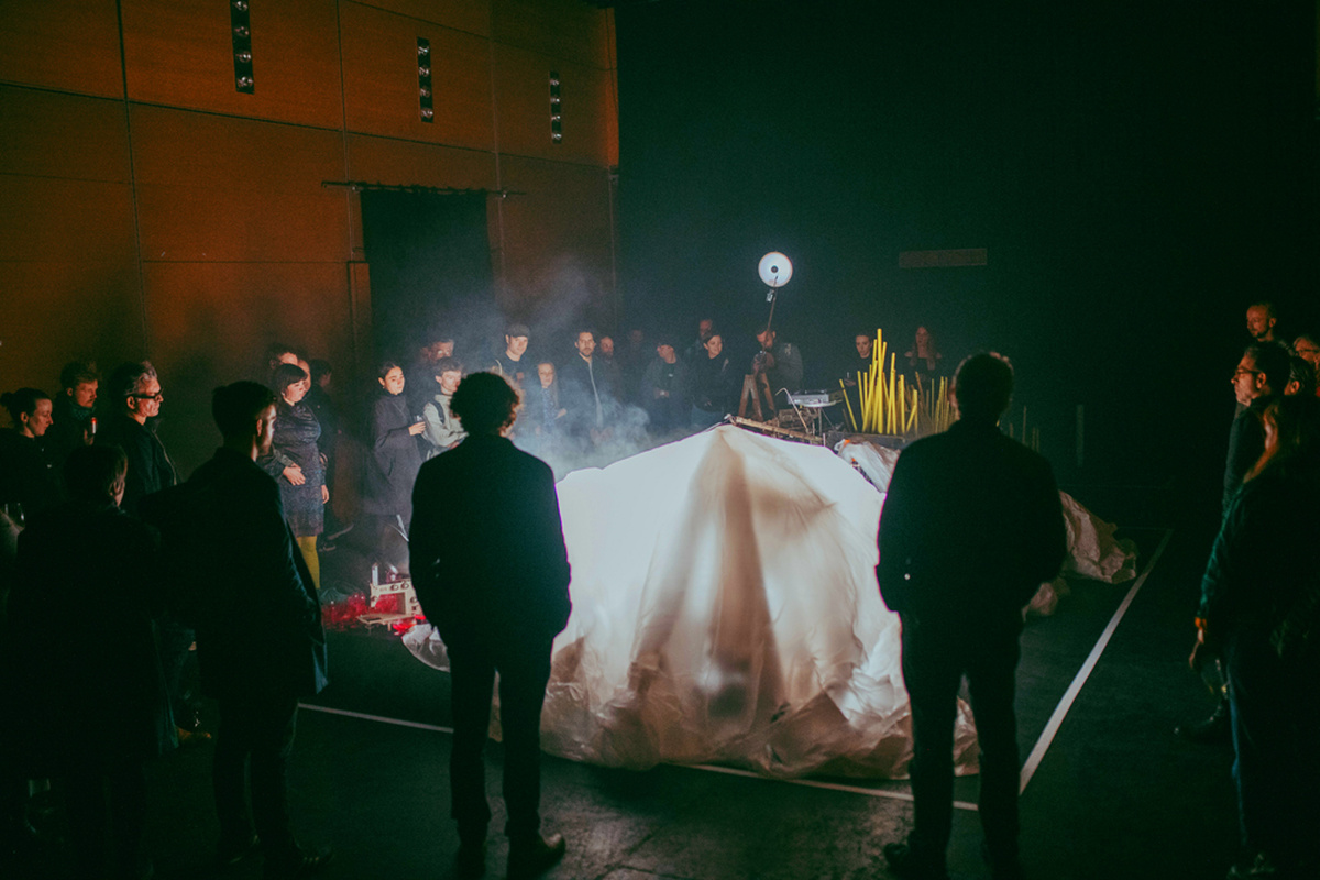 A circle of people in the CCA theatre look on to a large raised, lit up white sheet.