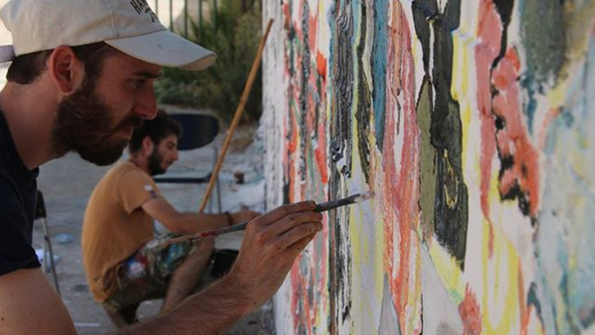 A close up of two people painting a white wall in Palestine with bright colours.