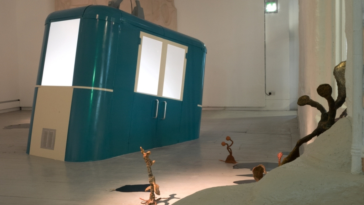 A gallery space featuring a large blue container that appears to be melting in to the floor.