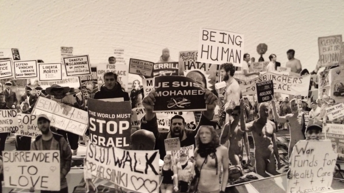 A sepia photo of a protest, many people hold up signs that state "Stop Israel" and "Surrender to Love".