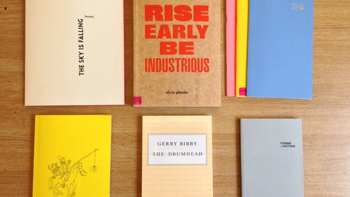 Six books with brightly coloured covers lie on a wooden table.