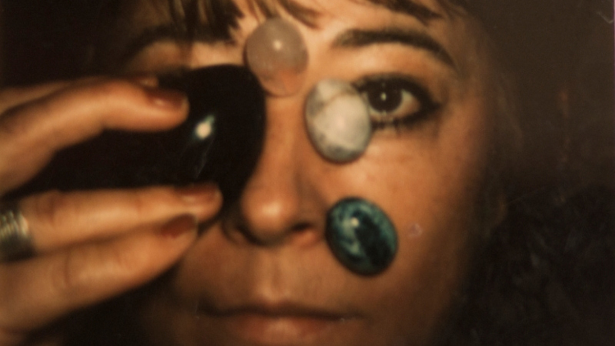 A close up of artist Ester Krumbachova holding four round stones on her face.