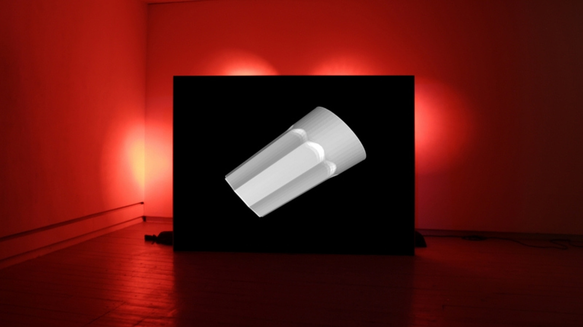 A dark room is lit up red, with a dark black screen in the centre of the room showing a rendering of a white object.